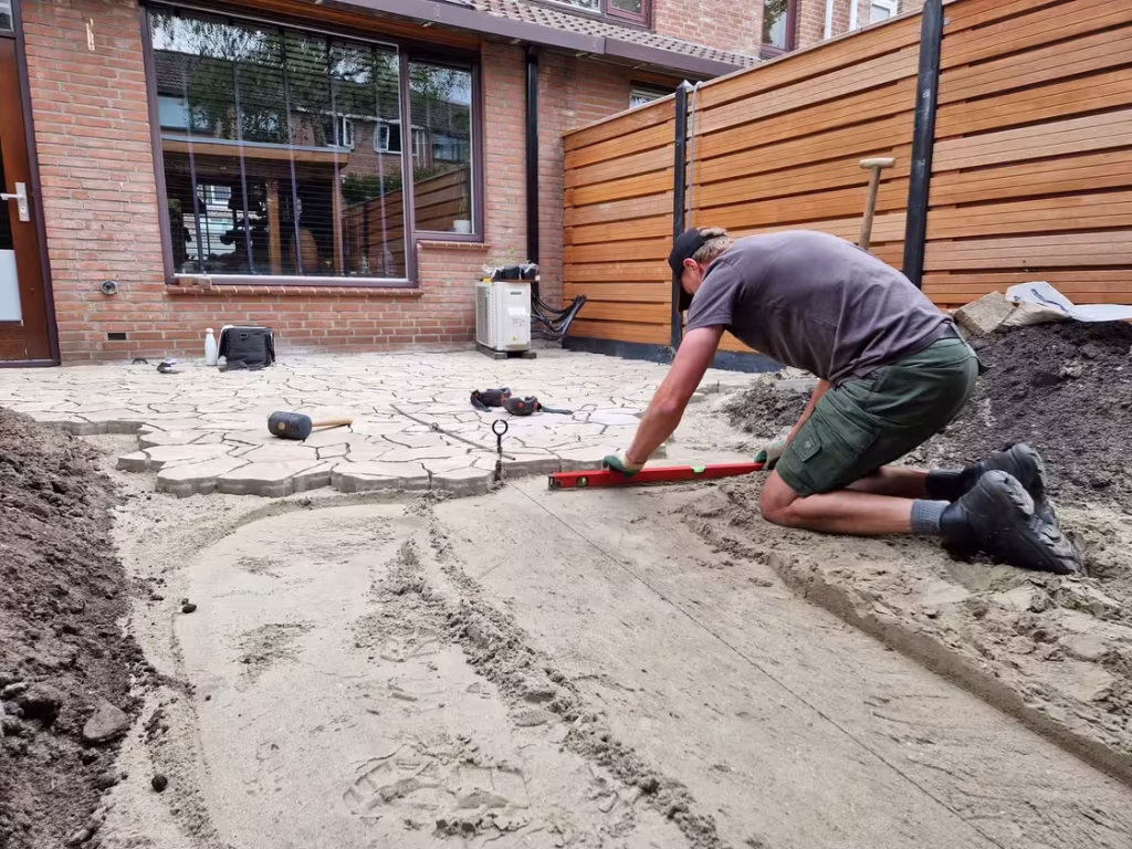 Hovenier maakt het pad waterpas en werkt aan de overgang tussen terras en tuin in Ommoord.