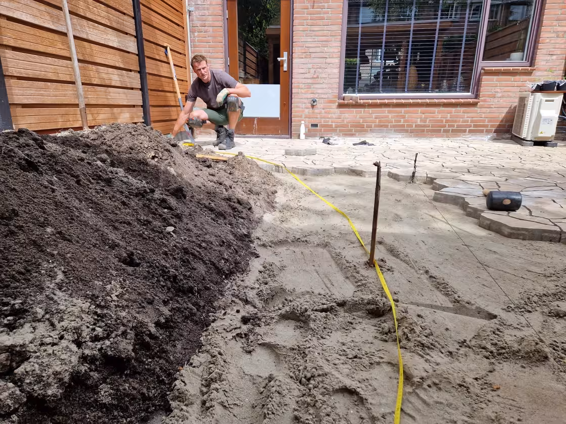 Hovenier bepaalt met een flexibel meetlint de juiste lijn voor de Cortenstaal border.