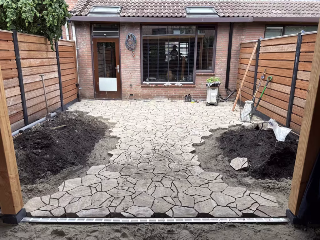 Overzicht van terras en pad richting het huis, inclusief afvoergoot onder de overkapping.