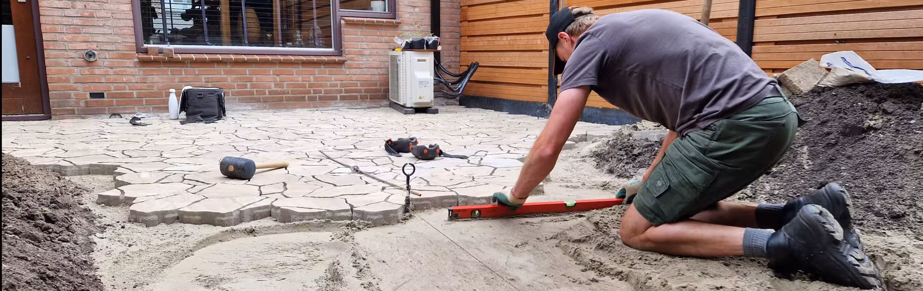 Hovenier maakt het pad waterpas en werkt aan de overgang tussen terras en tuin in Ommoord.
